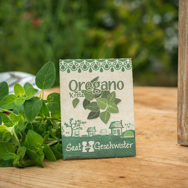 Oregano-Samentüte auf einem Holztisch neben frischen Oregano-Blättern.