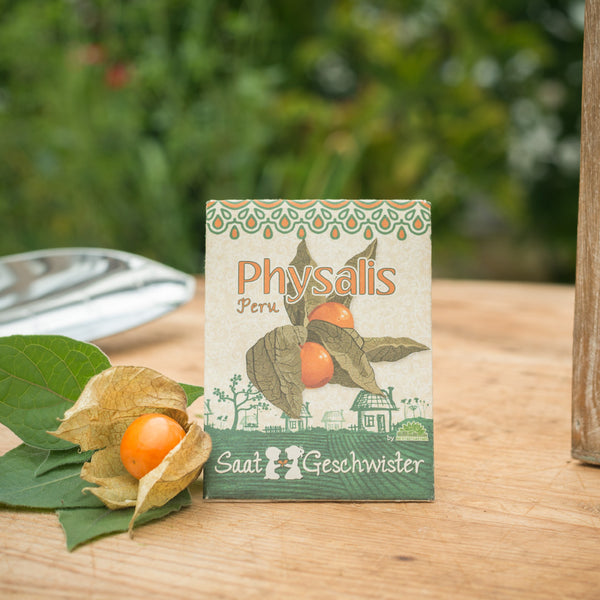 Samentüte für Physalis aus Peru mit einer geöffneten Frucht im Vordergrund auf einem Holztisch.