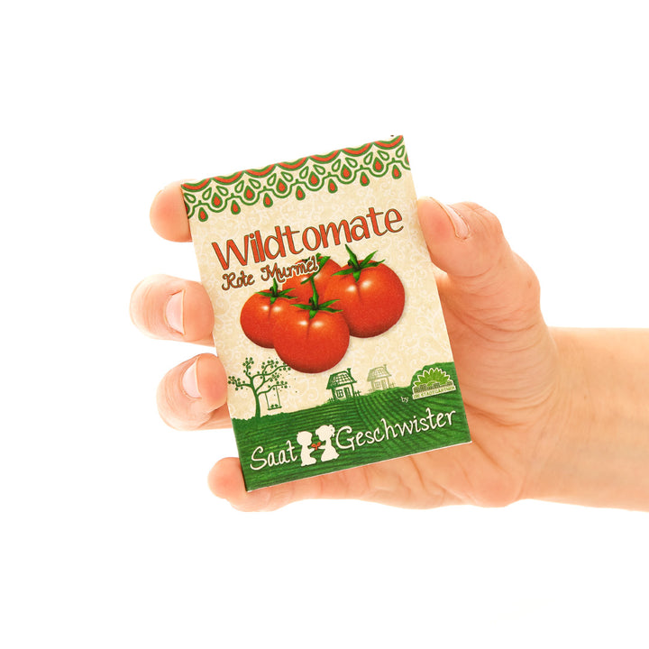 Eine Hand hält eine Saatguttüte für Wildtomaten mit der Aufschrift "Saat-Geschwister".