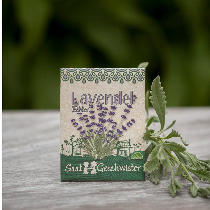 Lavendel-Samentüte auf einem Holztisch neben echten Lavendelblättern.