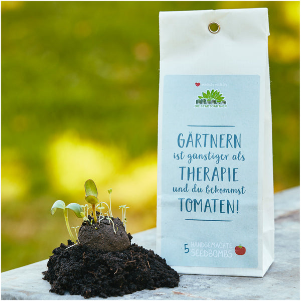 Produktverpackung für "Seedbombs" mit aufgehenden Pflänzchen und dem Slogan "Gärtnern ist günstiger als Therapie und du bekommst Tomaten!" auf unscharfem grünen Hintergrund.