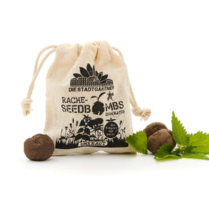 "Ein kleiner Jutebeutel mit Aufdruck 'DIE STADTGÄRTNER RACHE-SEEDBOMBS 100% NATUR' und ein paar Seedbombs neben frischen grünen Blättern auf weißem Hintergrund."