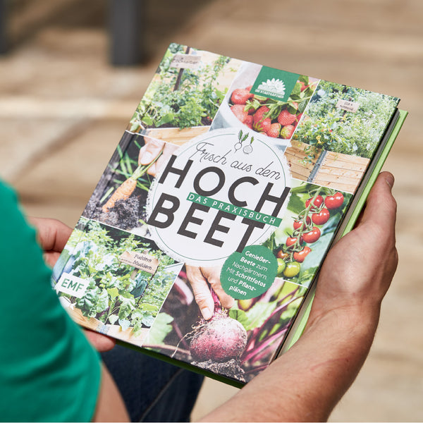 Person hält ein Gartenbuch mit dem Titel "Frisch aus dem Hochbeet" und verschiedenen Bildern von Gartenarbeit und Ernte.
