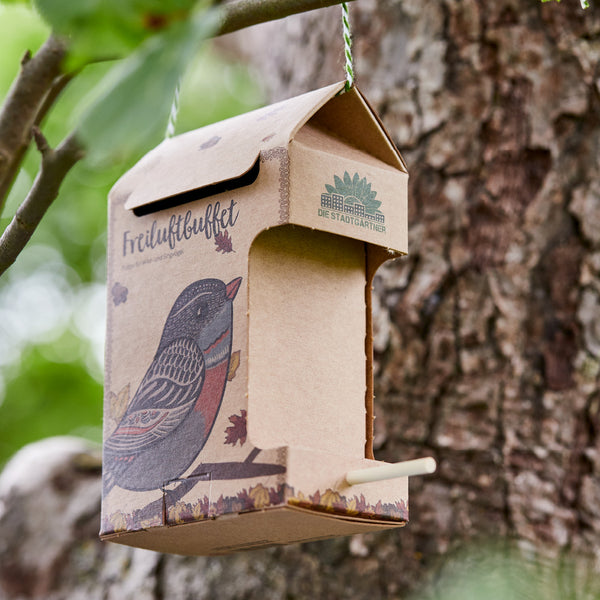 Kartonnist Vogelhaus mit Vogelillustration an einem Baum aufgehängt.