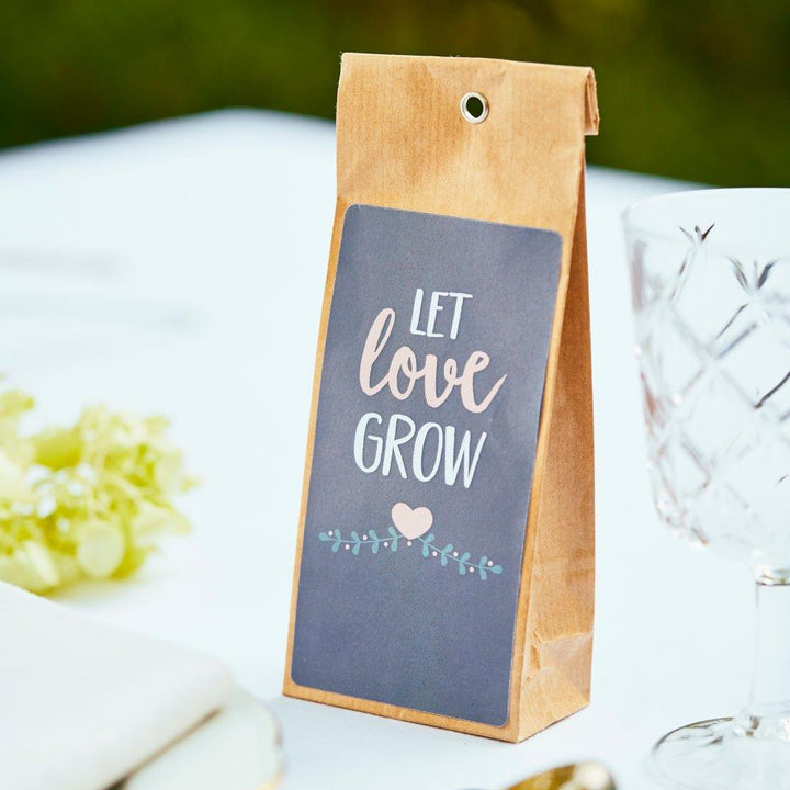 Braune Papiertüte mit Schriftzug "Let love grow" und Herzdekor auf einem festlich gedeckten Tisch.